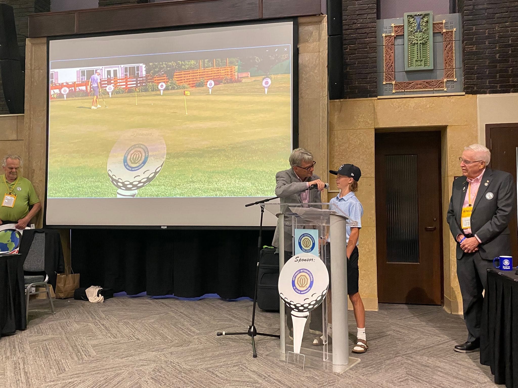 A junior golfer recognized at the podium during an Optimist Junior Golf presentation