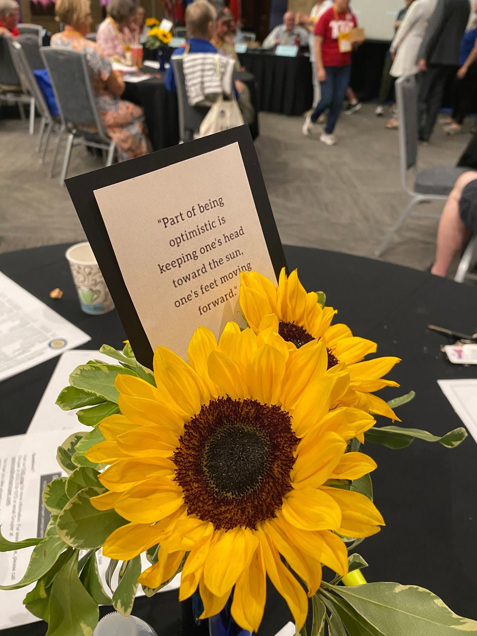 A sunflower centerpiece and a card sharing part of the Optimist Creed at a club meeting